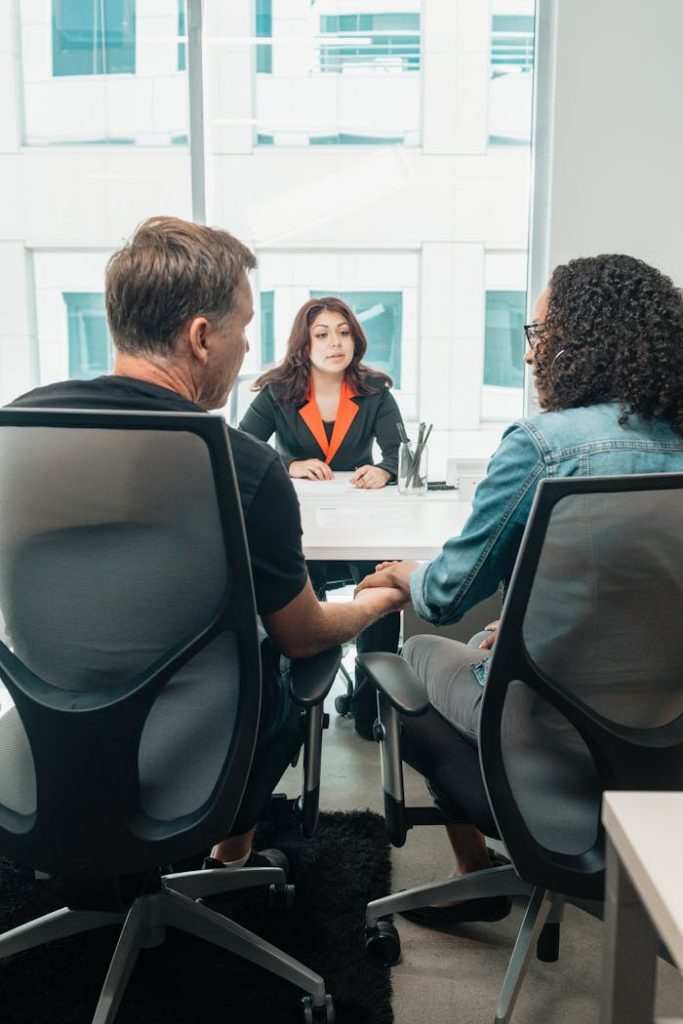woman-in-black-and-orange-blazer-sitting-by-the-table-7979446 A couple holding hands during a business consultation in a modern office setting.