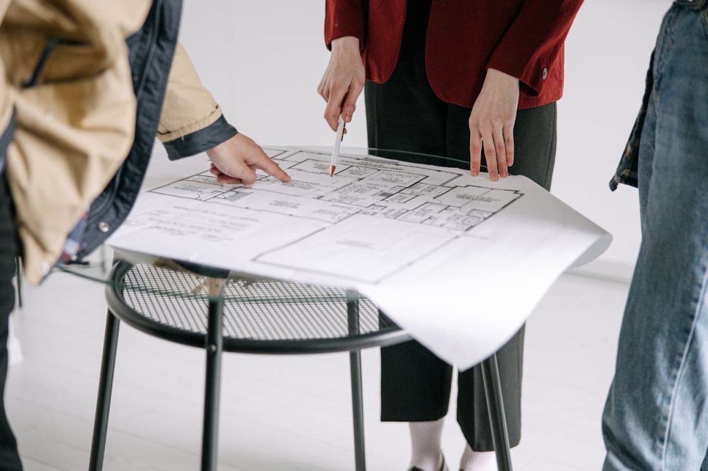 woman-pointing-at-blueprint-8962799 A group of people reviewing architectural blueprints on a table indoors.